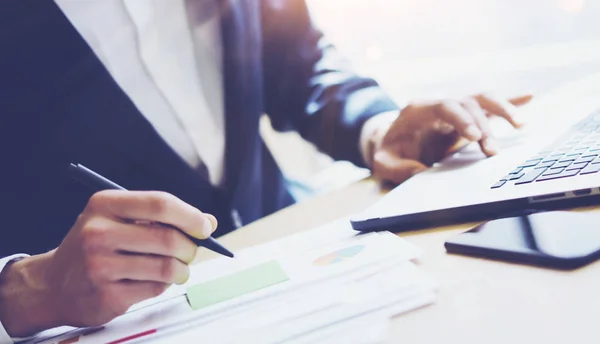 Homme d'affaires travaillant au bureau ensoleillé sur ordinateur portable.Homme pointant clavier portable et tenant la main stylo. Fond flou.Papaer documents sur la table . — Photo