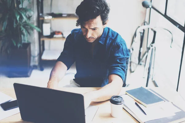 Aantrekkelijke jongeman werken bij zonnige office op laptop tijdens de vergadering op houten tafel. Zakenman analyseren digitale verslagen over zakboekje computer. Onscherpe achtergrond, horizontale. — Stockfoto