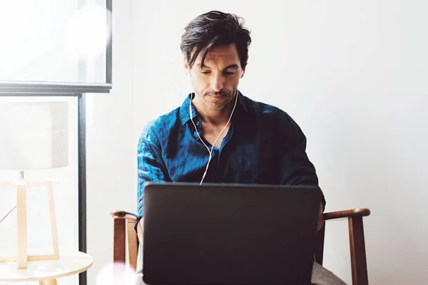 Uomo pensieroso in cuffia che lavora su laptop — Foto Stock