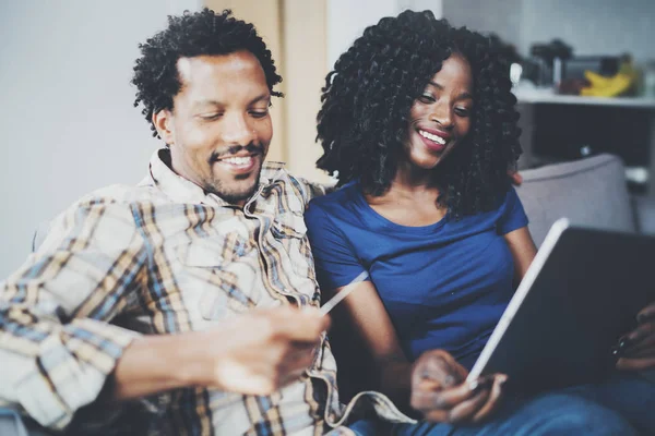 Glückliches junges afrikanisch-amerikanisches Paar, das zu Hause auf dem Sofa sitzt und online über einen mobilen Computer per Kreditkarte einkauft. horizontaler, verschwommener Hintergrund. — Stockfoto