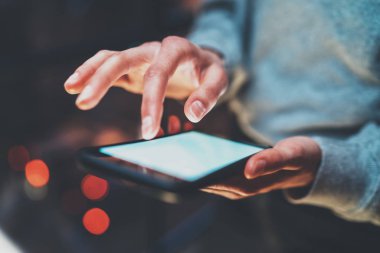 Modern smartphone elinde tutan kız closeup görünümü. Kız beyaz dokunmatik mobil ekranda geceleri yazarak. Yatay, bulanık arka plan, bokeh etkileri. Makro.