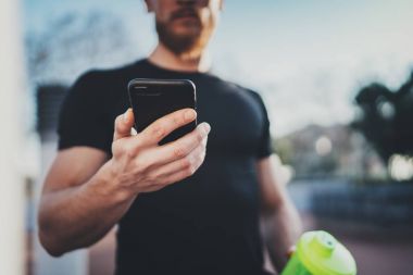 Smartphone uygulama ve akıllı izle yanık kalori iyi egzersiz oturum sonrası Şehir Parkı güneşli sabah kontrol kas yakışıklı sporcu. Arka plan bulanık.