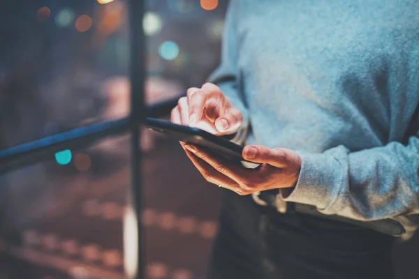 Close-up beeld van vrouw met moderne mobiele telefoon in handen. Meisje wijzen vingers op lege mobiele aanraakscherm bij nacht. Horizontale, onscherpe achtergrond, bokeh effecten. — Stockfoto