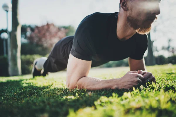 Outdoor Workout lifestyle concept.Young bearded man doing abdominal exercises before training.Muscular athlete exercising outside in sunny park. Blurred background.Horizontal. — Stock Photo, Image