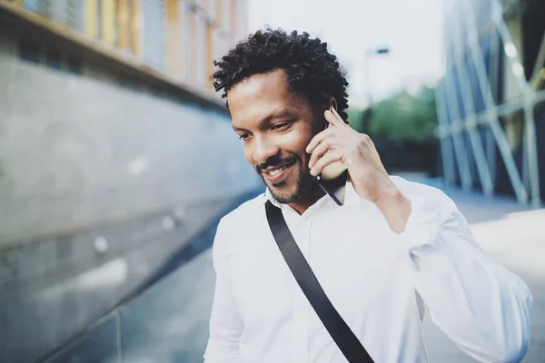 Sonriente hombre africano americano utilizando el teléfono inteligente para llamar a amigos en la calle soleada.Concepto de jóvenes jóvenes felices guapos disfrutando de gadgets al aire libre.Fondo borroso . — Foto de Stock