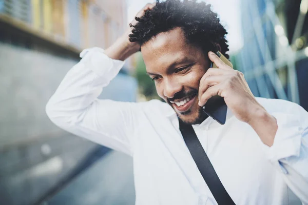Retrato de primer plano del hombre africano americano feliz usando el teléfono inteligente para llamar a amigos en la calle soleada.Concepto de gente joven y guapa feliz disfrutando de gadgets al aire libre.Fondo borroso . — Foto de Stock