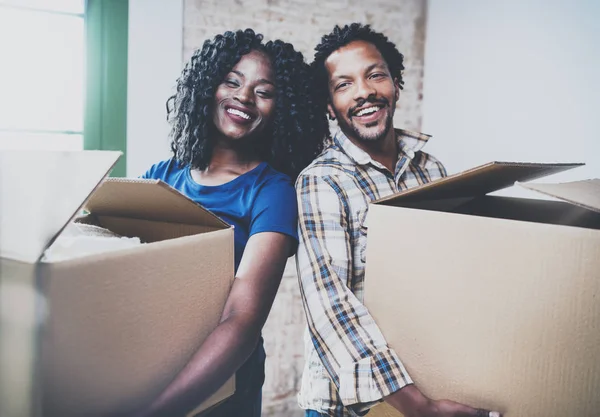 Happy young black african couple moving boxes into new house together and making a successful life.Cheerful family standing in empty new apartment.Horizontal.Blurred background.