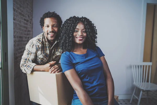 Young black african man and his girlfriend moving boxes into new house together and making a beautiful life.Cheerful family standing in empty new apartment.Blurred background. — Stock Photo, Image