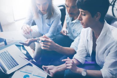 Ofiste dizüstü bilgisayar üzerinde çalışan üç genç arkadaşları. Tablet tutarak ve dokunmatik ekranda gösteren kadın. Yatay, bulanık arka plan. Kırpılmış.
