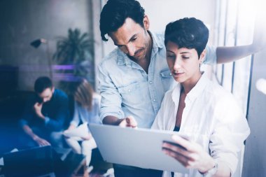 Grup genç iş ofis dizüstü bilgisayar üzerinde çalışıyor. Tablet tutarak ve dokunmatik ekranda gösteren kadın. Yatay, bulanık arka plan.