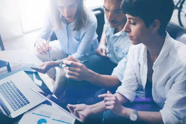 Ofiste dizüstü bilgisayar üzerinde çalışan üç genç arkadaşları. Tablet tutarak ve dokunmatik ekranda gösteren kadın. Yatay, bulanık arka plan. Kırpılmış.