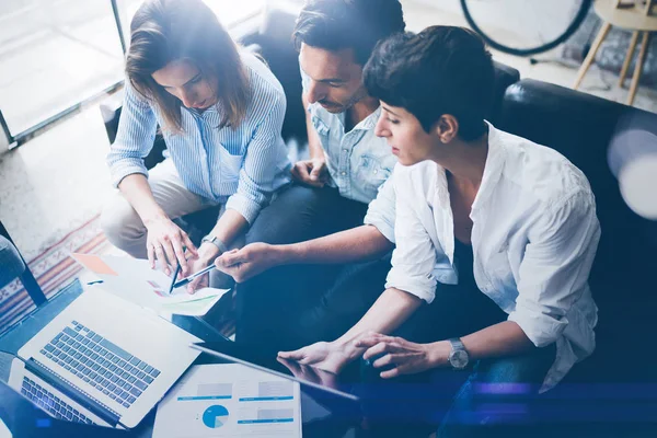 Ofiste dizüstü bilgisayar üzerinde çalışan üç genç arkadaşları. Tablet tutarak ve dokunmatik ekranda gösteren kadın. Yatay, bulanık arka plan. Üstten Görünüm.