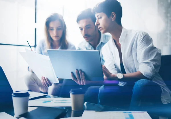 Drie jonge collega's werken op laptopcomputer op kantoor. Vrouw die tablet te houden en wijzen op touchscreen. Horizontale, onscherpe achtergrond. — Stockfoto