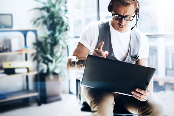 Businessman working at modern office on his digital tablet holding in hands.Attractive man wearing audio headset and making video conversation via digital tablet.Blurred background.