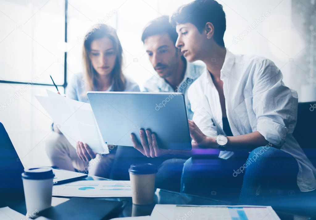 Three young coworkers working on laptop computer at office.Woman holding tablet and pointing on touch screen. Horizontal, blurred background.