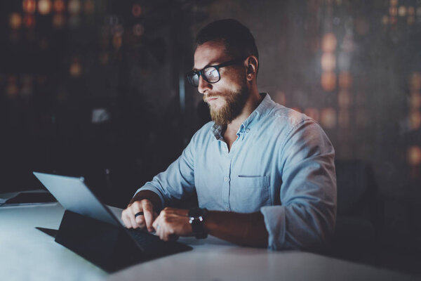 Bearded young colleorker working at night office e.Man using contemporary mobile tablet.Horizontal.Blurred background. Эффект вспышек и отражений
.
