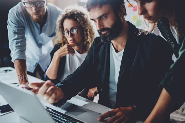 Coworkers working together in modern office e.Bearded man talking with colleague and using laptop while sitting at the wooden table.Horizontal.Blurred background . — стоковое фото