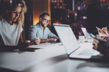 Grup genç iş arkadaşlarıyla birlikte iş vasıl gece modern iş yazıhane. Masada elektronik dizüstü bilgisayarlar kullanan gençlerin. Horizontal.Blurred arka plan.