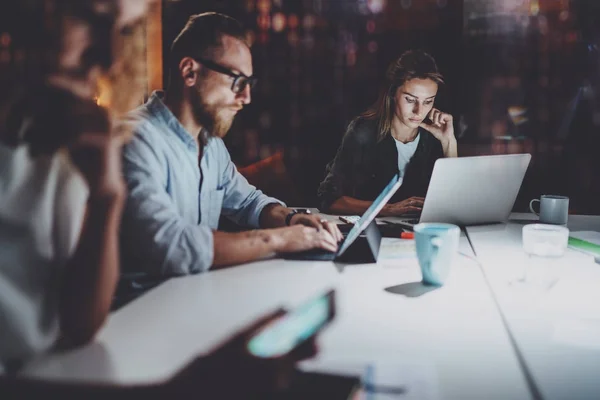 Un gruppo di giovani colleghi lavora insieme di notte.Giovani che utilizzano computer portatili elettronici al tavolo.Orizzontale.Sfondo sfumato . — Foto Stock