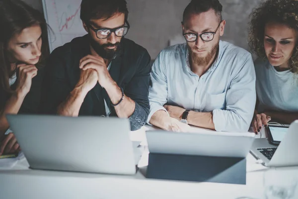 Grupo de jóvenes emprendedores que utilizan dispositivos móviles para buscar una solución empresarial durante el proceso de trabajo en la oficina nocturna. Fondo borroso. Horizontal . —  Fotos de Stock