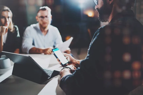 Współpracowników pracujących wspólnie w nowoczesne biuro. Brodaty mężczyzna rozmawia z kolegą i za pomocą mobilnego laptopa siedząc przy stole drewniane. Tło Horizontal.Blurred. Flary. — Zdjęcie stockowe