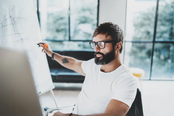 Homem barbudo jovem usando óculos e trabalhando no escritório ensolarado.Fundo borrado. Horizontal. Cultivadas . — Fotografia de Stock