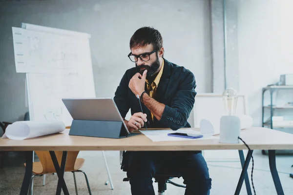 Un giovane architetto barbuto con occhiali da vista che lavora su un tablet digitale alla sua scrivania. Ingegnere esperto costruttore di progettisti professionisti.Horizontal.Sfondo sfocato . — Foto Stock