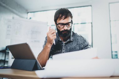 Modern ofis çatı katında çalışan yakışıklı sakallı tasarımcı. Elektronik kullanarak iş arkadaşınız güneşli işyeri tablet bilgisayarınızda dokunma. Yatay. Arka plan bulanık.