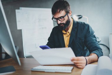 Ahşap masada otururken bilgisayarda lightful ofisinde çalışan genç iş arkadaşınız. Adam ellerini ve onun smartphone kontrol belgesi analiz. Arka plan bulanık. Horizontal.Cropped.