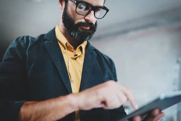 Bearded handsome coworker working at lightful office.Man using contemporary mobile digital tablet.Horizontal.Blurred background.Cropped. — Stock Photo, Image