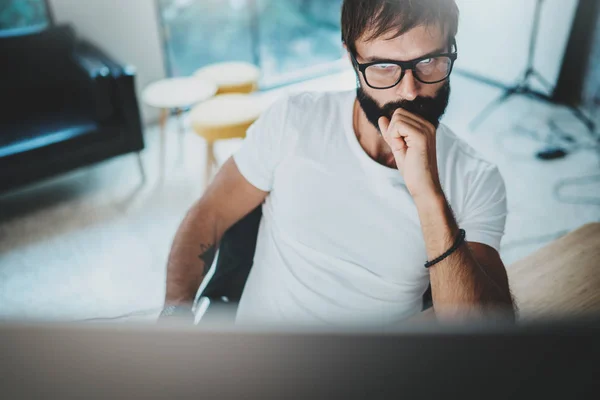 Giovane uomo barbuto che indossa occhiali da vista e lavora in un moderno studio-ufficio loft. Orizzonte . — Foto Stock