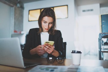 Ofiste çalışırken genç işkadını yazarak kısa mesaj smartphone cep telefonu ile gülümseyen. Arka plan bulanık.
