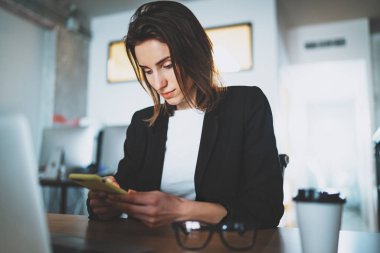 Ofiste çalışırken Smartphone'da kısa mesaj yazarak bir iş kadını. Arka plan bulanık.