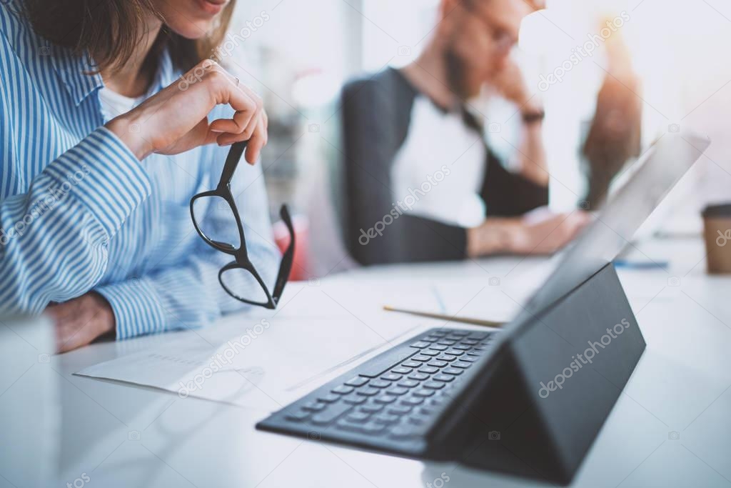 Teamwork concept.Young woman working with colleagues and holding eyes glasses at hand.Horizontal.Blurred background.