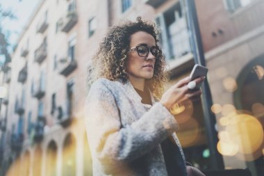 Sırasında akıllı telefonu, mobil şebeke bilgilerinde arama Hansome kız hipster gözlük Avrupa şehirde yürümek. Bokeh ve mercek parlamaları arka plan bulanık üzerindeki etkileri.