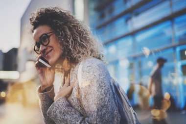 Gülümseyen kadın gece sokakta duran onun hücre telefon ile mobil telefon görüşmesi. Arka plan bulanık bokeh ve mercek parlamaları etkisi.