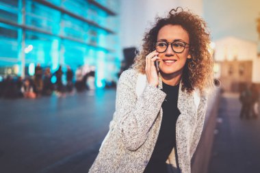 Gülümseyen kadın gece sokakta duran onun hücre telefon ile mobil telefon görüşmesi. Arka plan bulanık bokeh ve mercek parlamaları etkisi.