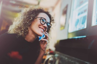 Güzel gülümseme yapım seslenmek yolu ile cep telefonu kafede dinlenme sırasında büyüleyici kadınla. Arka plan bulanık bokeh ve mercek parlamaları etkisi.