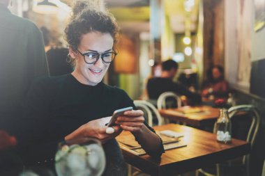 Sevimli kadın güzel gülümsemeyle kafede dinlenme sırasında cep telefonu kısa mesaj okuma. Arka plan bulanık bokeh ve mercek parlamaları etkisi.