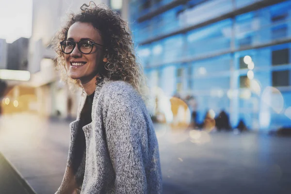 Beautiful woman in stylish clothing wearing eye glasses outside in the european night city. Bokeh and flares effect on blurred background. — Stock Photo, Image