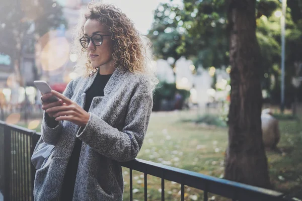 Mujer hipster con mochila y gafas buscando información en la red móvil por teléfono inteligente, durante el paseo en el parque de la ciudad europea. Efectos de bokeh y bengalas sobre fondo borroso . —  Fotos de Stock