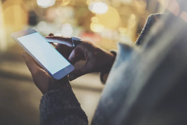 Meisje wijzende vinger op scherm smartphone in de sfeervolle stad nacht. Vrouwelijke handen SMS bericht mobiele telefoon. Close-up op onscherpe achtergrond. Fakkels, bokeh effecten. — Stockfoto