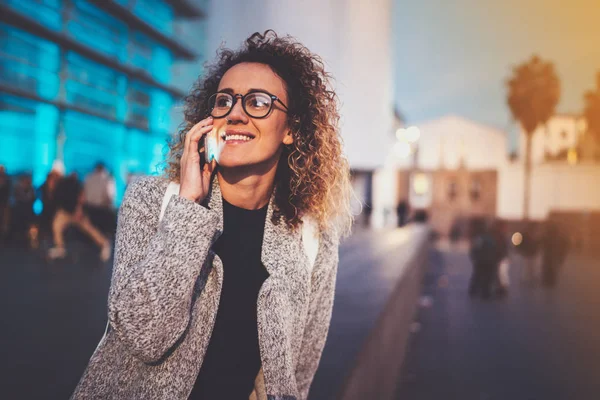 Femme souriante passer un appel mobile avec son téléphone portable tout en se tenant debout la nuit dans la rue. Effet Bokeh et fusées éclairantes sur fond flou . — Photo