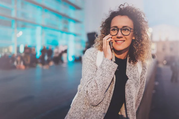 Lachende jong meisje met haar mobiele telefoon terwijl je 's nachts op straat roepen. Bokeh en fakkels effect op onscherpe achtergrond. — Stockfoto