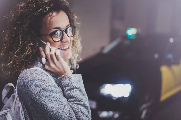 Vrouw toeristische dragen bril aanroepen van taxiservice door de telefoon van de cel, tijdje staat op straat in de nacht. Effecten van bokeh en vuurpijlen op onscherpe achtergrond. — Stockfoto