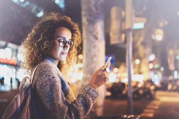 Mooi meisje hipster bril hand in hand slimme telefoon, tijdens de nacht wandelen in Europese roeping. Effecten van bokeh en vuurpijlen op onscherpe achtergrond. — Stockfoto