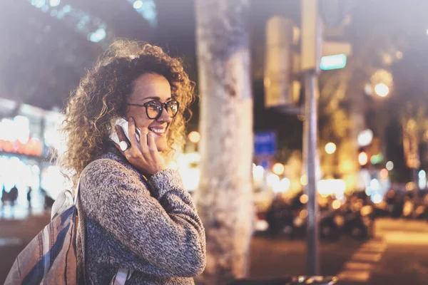 Mooie vrouw maken gesprek oproep lachend met haar vrienden via mobiele telefoon terwijl je 's nachts op straat. Bokeh en fakkels effect op onscherpe achtergrond. — Stockfoto