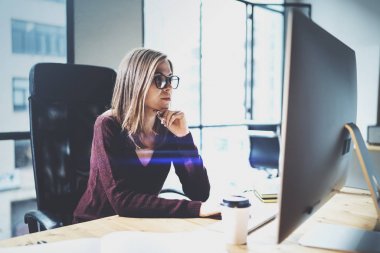 Çekici genç iş kadını ofiste modern çalışma yerde masaüstü bilgisayar kullanarak. Arka plan bulanık. Yatay.