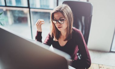 Çekici genç iş kadını ofiste modern çalışma yerde masaüstü bilgisayar kullanarak. Arka plan bulanık. Yatay.