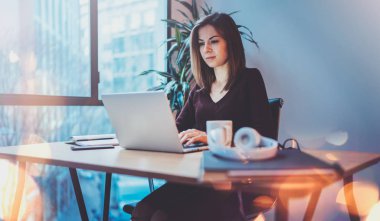 Dizüstü bilgisayarda gece ofiste onun işyerinde çalışan genç çekici kız. Horizontal.Blurred arka plan. Mercek parlamaları.